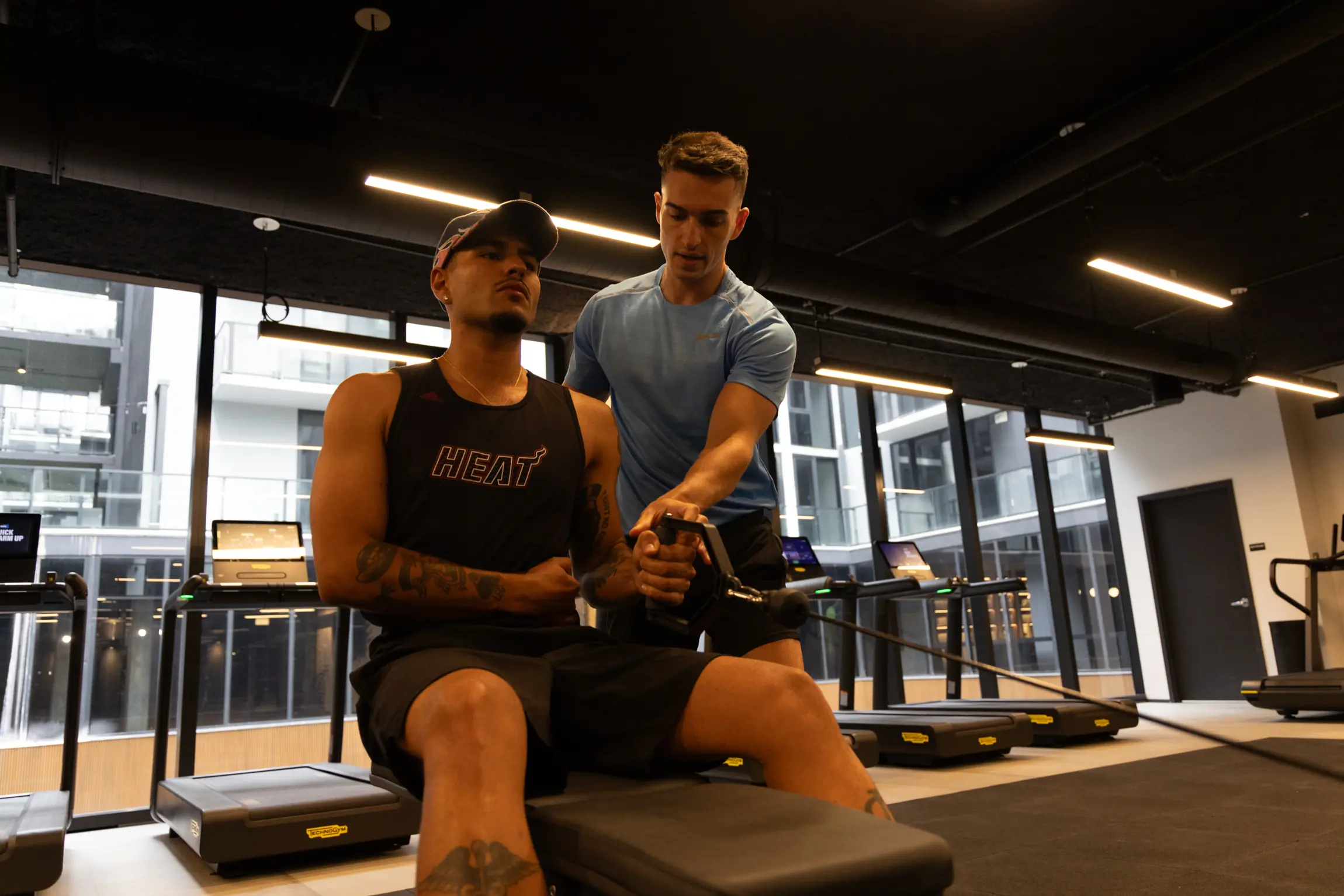 Entrenador personal guiando a un cliente en un remo en polea en un gimnasio privado de Miami